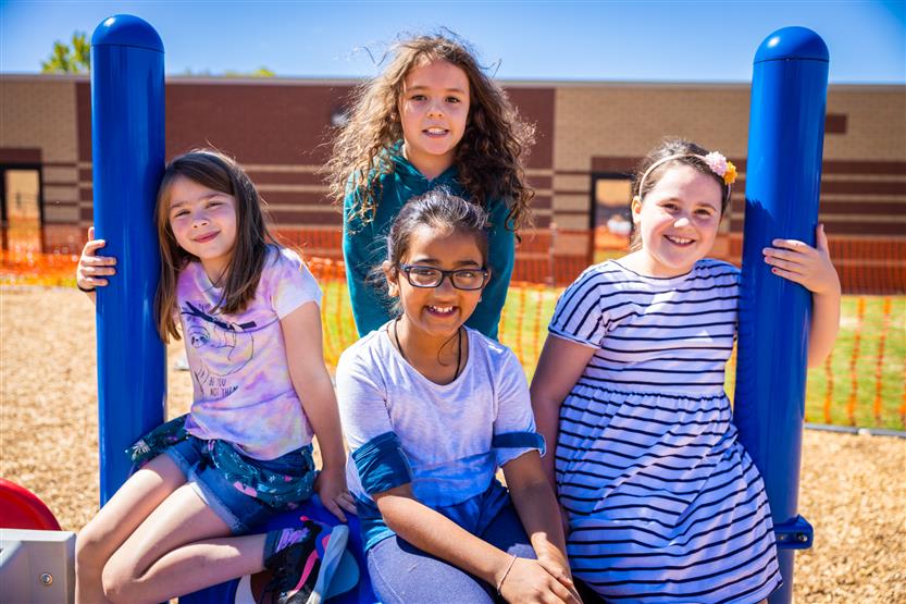 Four girls smile while sitting on playground equipment
